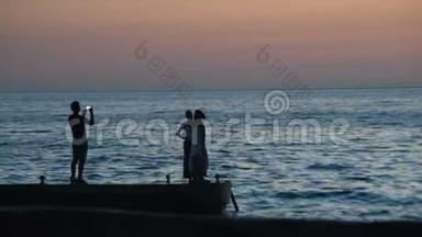 日落时分，男人在海滩上给两个女人拍照